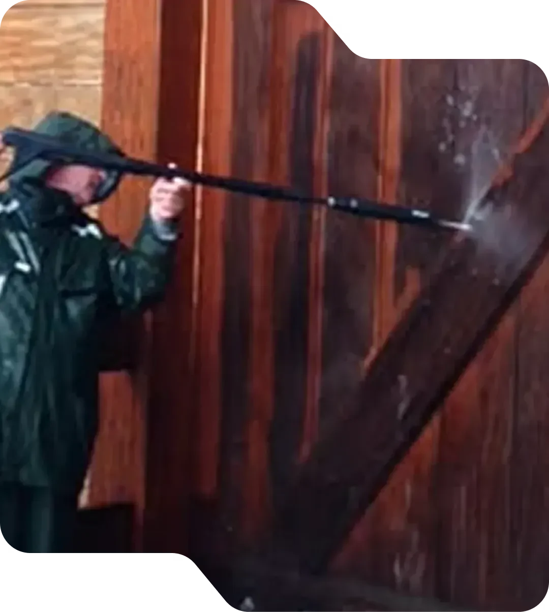 Medewerker reinigt een houten deur met een hogedrukspuit